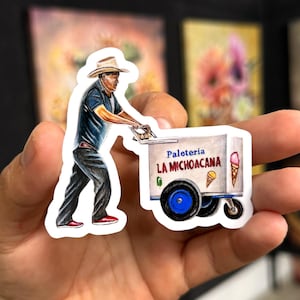 May include: A sticker featuring a detailed illustration of a person pushing an ice cream cart. The cart has the text "Paleteria La Michoacana" and images of ice cream cones. The person is wearing a hat and dark clothing.