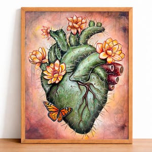 Puede incluir: Una obra de arte enmarcada representa un cactus verde en forma de corazón adornado con flores naranjas y una mariposa. La obra de arte tiene un marco de madera y está sobre un fondo suave y colorido. El cactus tiene espinas y un sistema vascular detallado.