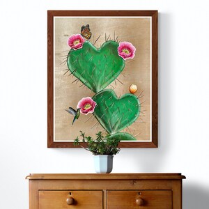 May include: A framed painting of a heart-shaped cactus with pink flowers and a hummingbird. The cactus is green and has spines. The background is a light brown color.
