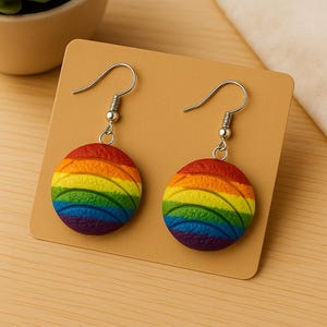May include: A pair of rainbow-colored earrings. Each earring features a round, layered design in the colors of the rainbow: red, orange, yellow, green, blue, and purple. The earrings have silver-colored hooks.