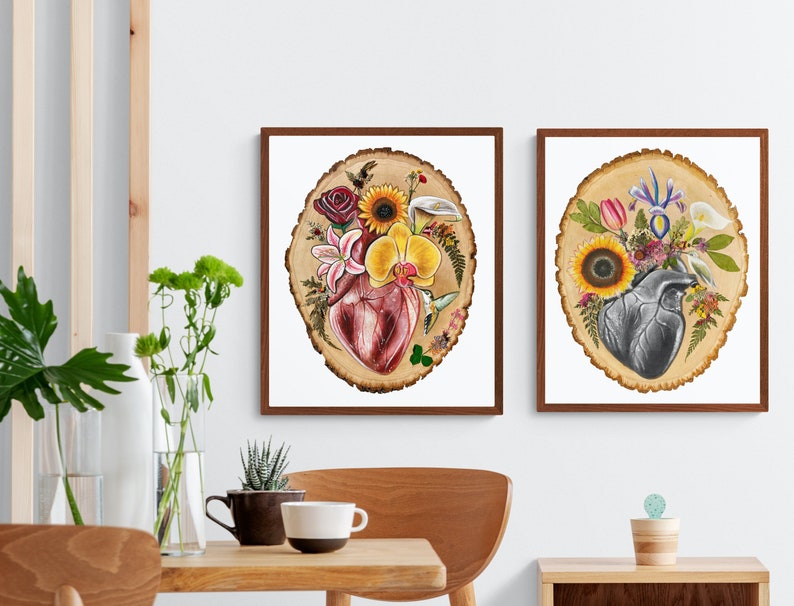 May include: Two framed prints of anatomical hearts surrounded by flowers and greenery on a wood slice background. The heart on the left is red and the heart on the right is gray.