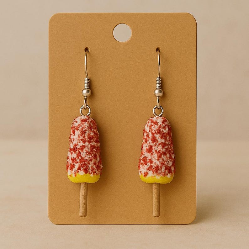May include: Novelty earrings in the shape of red and white ice lollies with yellow bases and wooden sticks. The earrings are suspended from silver-coloured fish hook ear wires and presented on a brown earring card.