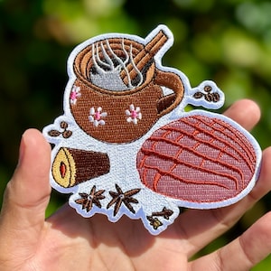 May include: Embroidered patch featuring a brown clay mug with a cinnamon stick and steam, a pink and brown concha bread, and brown cinnamon sticks and star anise.