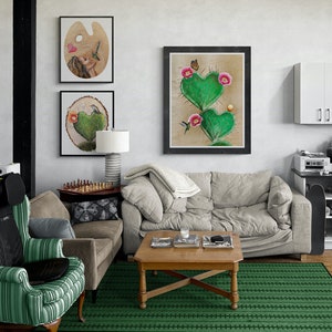 May include: A living room interior with a green rug, a light grey sofa, a coffee table with books, and three framed pictures on the wall. The pictures feature a woman, a heart-shaped cactus, and a paint palette.