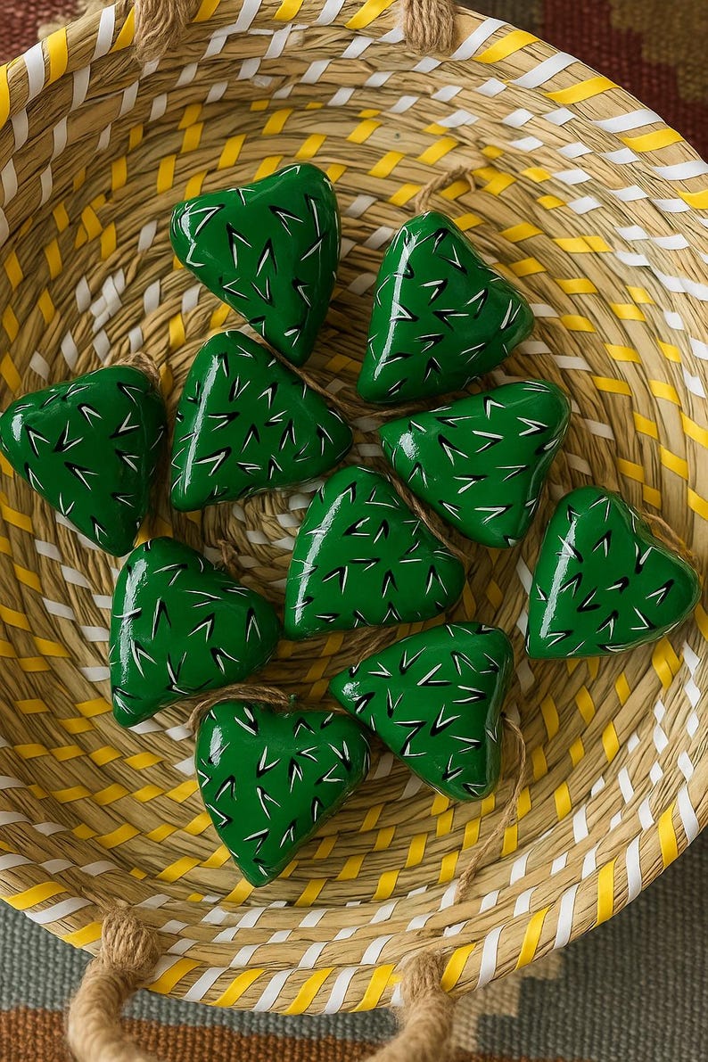 May include: A collection of ten heart-shaped ornaments with a vibrant green finish, adorned with white and black linear details, resting inside a woven basket with yellow and white stripes. Each ornament is suspended by a natural twine loop.