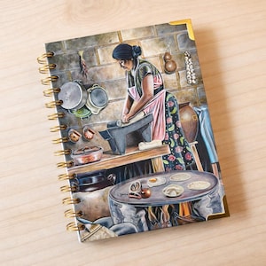 May include: Spiral-bound notebook with a watercolour illustration of a woman in a kitchen preparing food. The artwork depicts a traditional cooking scene with a woman making tortillas, with pots, pans, and a cooking fire. The notebook has gold-coloured corner protectors and spiral binding.
