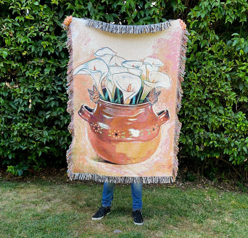 May include: A woven tapestry wall hanging featuring a terracotta pot filled with white calla lilies and butterflies. The pot has a brown and white design.