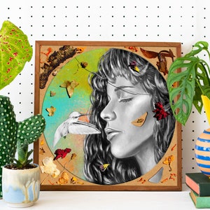May include: A framed mixed media artwork featuring a black and white portrait of a woman with her eyes closed. The woman's face is surrounded by a circle of dried flowers and leaves, including a hummingbird in flight. The artwork has a rustic, natural feel.