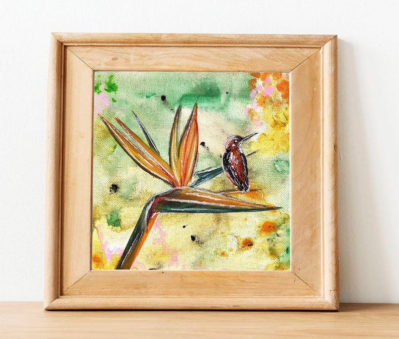 May include: A framed painting of a bird perched on a vibrant orange and yellow bird of paradise flower. The background is a watercolor wash of green, yellow, and pink.