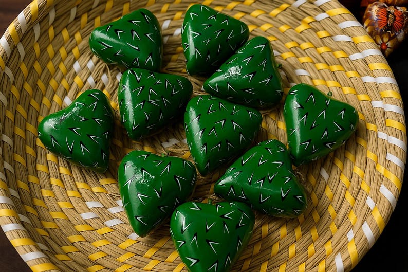 May include: A collection of green heart-shaped ornaments with white accents, resembling cacti, are arranged in a woven basket. The basket has a yellow and white pattern. The ornaments are likely handmade and decorative.