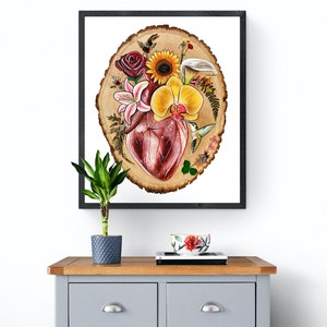 May include: A framed print of a watercolor painting depicting a human heart surrounded by flowers and a hummingbird on a wood slice background.