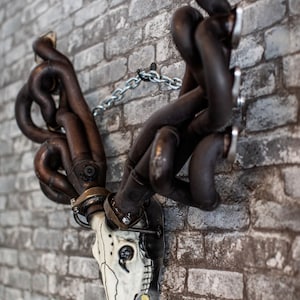 May include: A white deer skull mounted on a brick wall with a metal chain and a set of black exhaust manifolds forming the antlers.