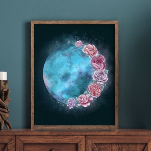 May include: A framed print of a blue crescent moon with pink and white flowers around it. The print is hanging on a dark blue wall above a wooden cabinet.
