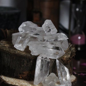 Peut inclure: Un groupe de cristaux de quartz transparents disposés sur une plate-forme en bois. Les cristaux sont de différentes tailles et formes, certains étant pointus et d'autres plus arrondis. Les cristaux sont éclairés par une lumière douce, mettant en valeur leur beauté naturelle.