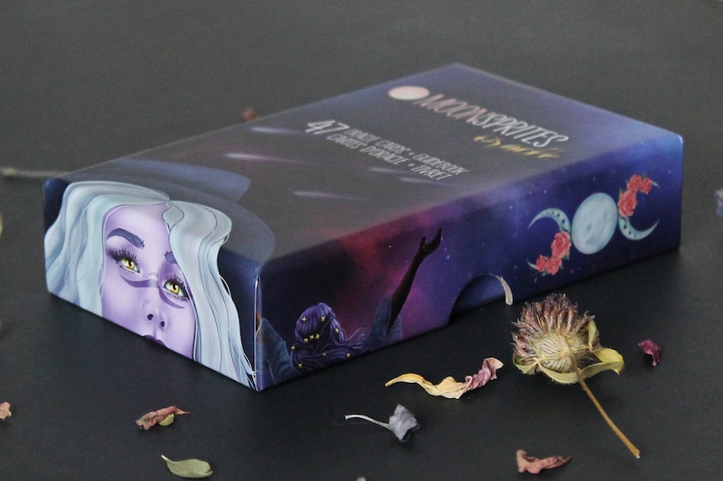 May include: A box of Moon Sprites Oracle Cards with a purple and blue design featuring a woman with long white hair and a crescent moon with roses. The box has the text "Moon Sprites Oracle" and "47 Cards - Guidance - Growth - Inner Strength - Tarot".