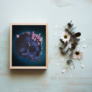 May include: A framed illustration of a dark blue skull with pink crystals on top. The skull is set against a dark blue background. The frame is made of wood and has a light brown finish.