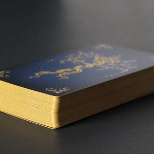 May include: A deck of playing cards with a gold gilded edge and a blue back with a gold design of a tree.