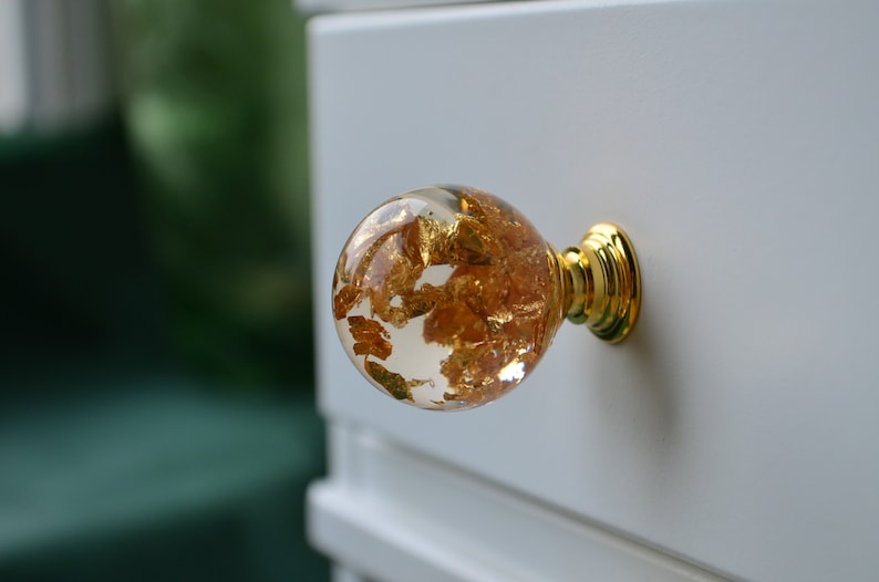 May include: A round, clear glass cabinet knob with gold leaf accents and a gold metal base.