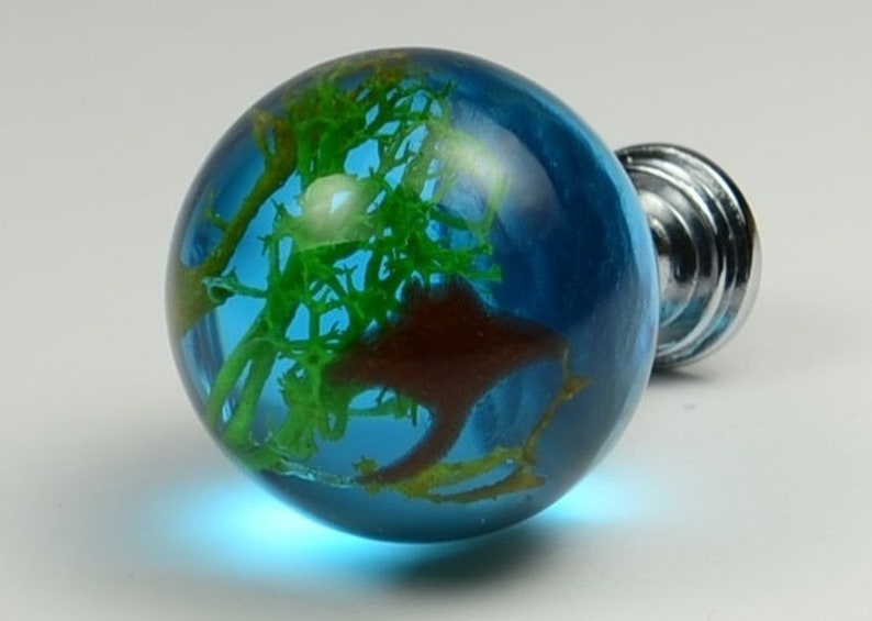 May include: A blue glass globe with green and brown inclusions, mounted on a silver knob. This decorative knob is perfect for adding a unique touch to furniture.
