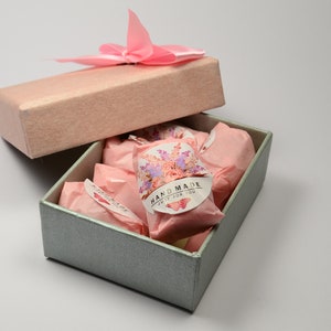 May include: A light blue gift box with a pink lid and a pink bow. The box is open and contains several small pink packages with floral designs and the text "HAND MADE JUST FOR YOU".