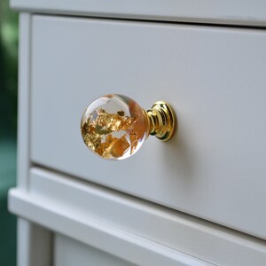 May include: A clear glass drawer knob with gold leaf accents and a brass base.