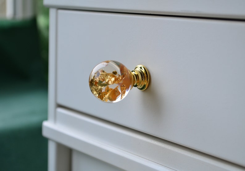 May include: A clear glass drawer knob with gold leaf accents and a brass base.
