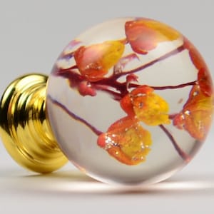 May include: A clear glass sphere with a gold base, containing dried red and yellow flowers. The sphere is about 1 inch in diameter.