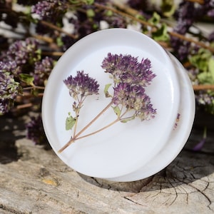 May include: A white round resin coaster with a pressed purple flower design.