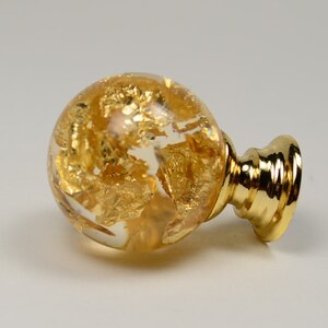 May include: A gold-toned cabinet knob with a clear glass sphere containing gold leaf accents. The knob has a round base.