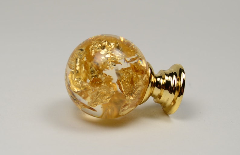 May include: A gold-toned cabinet knob with a clear glass sphere containing gold leaf accents. The knob has a round base.