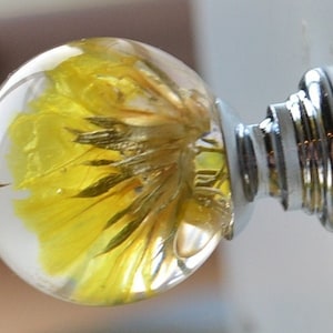 May include: A clear glass knob with a yellow flower encased inside. The knob has a silver metal base.