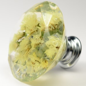May include: A clear glass cabinet knob with a faceted diamond shape. The knob is filled with dried yellow flowers.
