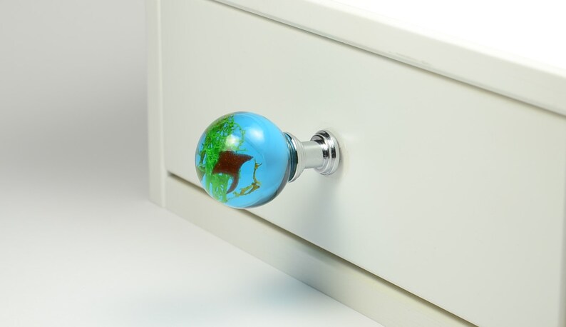 May include: A blue and green globe-shaped drawer pull with a chrome base. The pull is attached to a white drawer.