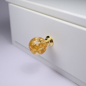 May include: A gold-toned drawer pull with a clear glass sphere filled with gold leaf accents.