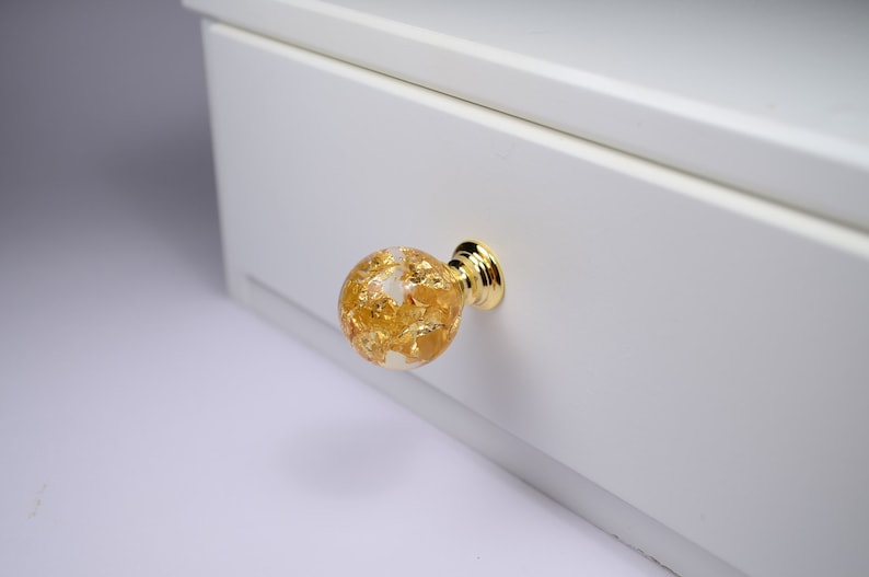 May include: A gold-toned drawer pull with a clear glass sphere filled with gold leaf accents.