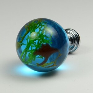 May include: A blue glass cabinet knob with a green and brown resin design inside. The knob has a silver base.