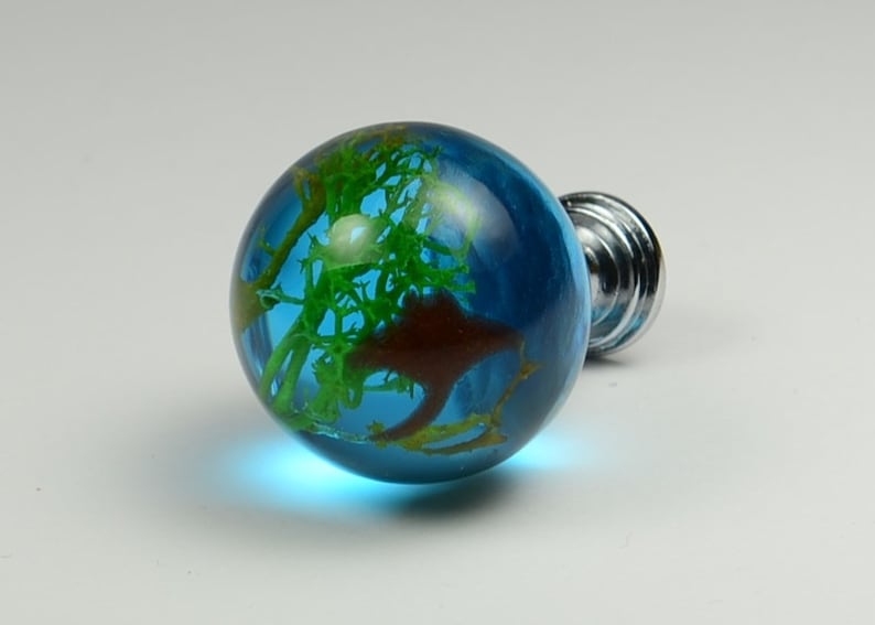 May include: A blue glass cabinet knob with a green and brown resin design inside. The knob has a silver base.