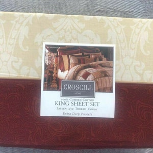May include: A folded king sheet set with a cream-colored top featuring a white floral pattern. The bottom section is a deep red with a paisley design. The product label reads "CROSCILL HOME KING SHEET SET".