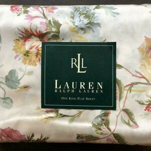 Può includere: Un lenzuolo piatto bianco con un motivo floreale in tonalità di rosa, verde e giallo. Il lenzuolo presenta un'etichetta con il testo "LAUREN RALPH LAUREN" e "One King Flat Sheet".
