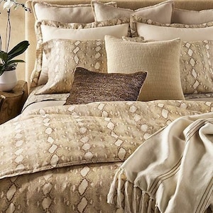 May include: A beige and brown patterned bedding set with a throw blanket. The bedding features a snake skin pattern. The throw blanket is a solid beige color.