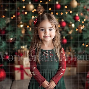 May include: A young girl wearing a green dress with red embroidered sleeves stands in front of a Christmas tree decorated with red ornaments and lights.