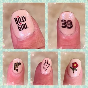 May include: A collage of five fingernails, each painted light pink with different designs. One nail features the text "BILLY GIRL" with a heart, another has the number "33", and the others display a fish, a goat head, and a red flower.
