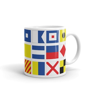 May include: White ceramic mug displaying a grid of nautical signal flags in various colours, including blue, red, yellow, and black. The flags are arranged in a grid pattern around the mug's exterior. The mug has a white handle.