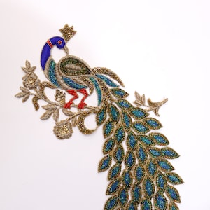 May include: A gold, blue, and green beaded peacock applique with a crown on its head. The peacock is perched on a branch with gold and green leaves.