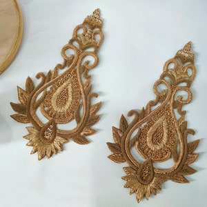 Peut inclure: Deux appliques en tissu de forme paisley ornées, de couleur dorée, avec des broderies et des paillettes complexes.