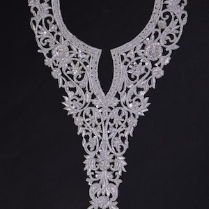 Op de afbeelding: Zilveren geborduurde halslijn applicatie met bloemen- en bladerpatronen. De applicatie heeft ingewikkelde details en is versierd met pailletten. Het ontwerp is symmetrisch en geschikt voor het verfraaien van kleding.