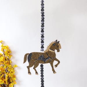 May include: A beaded horse figurine with a black and gold color scheme. The horse is standing on a black beaded chain.