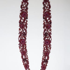 May include: Two burgundy-colored floral lace appliques. Each applique features a repeating pattern of roses and leaves, with a darker shade of burgundy in the center of the flowers. The appliques are symmetrical and curved.
