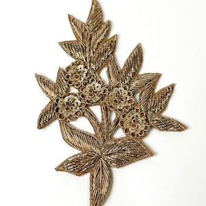 Może przedstawiać: Złota haftowana aplikacja kwiatowa z wzorem liści. Aplikacja wykonana jest z cekinów i koralików.