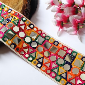 May include: A decorative trim with a cream-colored base, featuring colorful embroidery and mirrored accents. The design includes geometric shapes in pink, orange, yellow, green, and blue. The trim is approximately 2 inches wide.